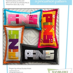May include: Four colorful pincushions shaped like the word "PINS". Each pincushion is made of patchwork fabric and has a different color scheme. The pincushions are arranged in a row, with the word "PINS" spelled out. The pincushions are 3 3/4 inches by 7 3/4 inches.