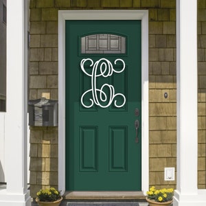 May include: A white, cursive monogram letter is mounted on a dark green front door. The door has a glass panel at the top and is flanked by white columns and a mailbox. Yellow flowers in a terracotta pot sit at the base of the door.