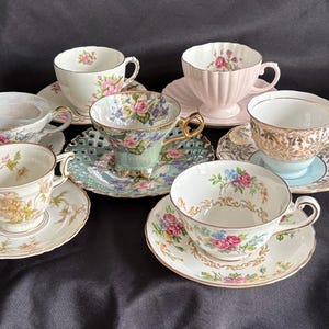 May include: A collection of vintage teacups and saucers. The cups feature various floral patterns and colors, including pink, blue, and gold. Some cups have intricate designs and textures, while others are more simple. The saucers complement the cups with matching or coordinating patterns.