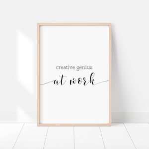 Puede incluir: Una impresión enmarcada con el texto "creative genius at work" en fuente cursiva negra sobre un fondo blanco.