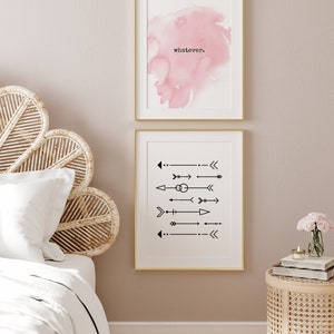 May include: Two framed art prints. The top print features a pink watercolor wash with the word "whatever" in black. The bottom print displays black arrow designs on a white background, both framed in gold.