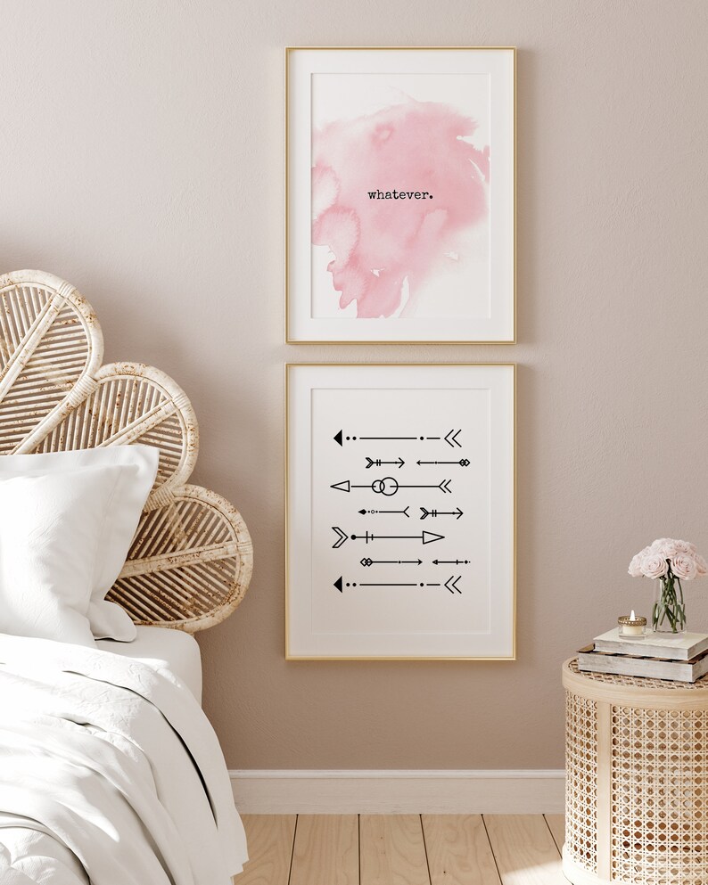 May include: Two framed art prints. The top print features a pink watercolor wash with the word "whatever" in black. The bottom print displays black arrow designs on a white background, both framed in gold.