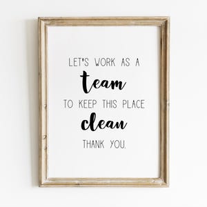 May include: A rectangular wall sign in a light brown wooden frame featuring black text on a white background that reads: LET'S WORK AS A team TO KEEP THIS PLACE clean THANK YOU. The sign is oriented vertically and has a simple, clean design.