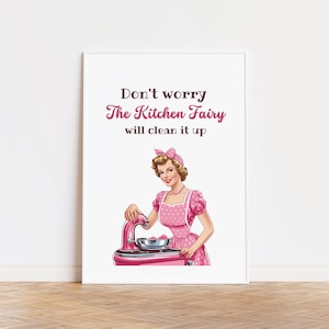 May include: A white framed print with a pink and white illustration of a woman in a pink polka dot dress and apron. The text on the print reads "Don't worry The Kitchen Fairy will clean it up."