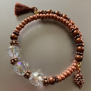 May include: A copper and crystal bracelet with a tassel and a pine cone charm. The bracelet is made with small copper beads and clear crystal beads.