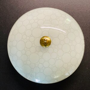 May include: A round, frosted glass ceiling light fixture with a brass center knob. The glass shade features a pattern of overlapping circles in varying sizes. The fixture is designed to be mounted on a ceiling.