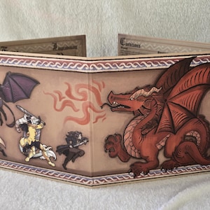 Puede incluir: Una pantalla plegable para juegos de mesa con fondo color canela que muestra un gran dragón rojo lanzando fuego a tres aventureros. El lado izquierdo muestra una criatura alada, un arquero y un guerrero con espada. Hay texto visible arriba.