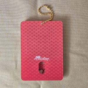 May include: A rectangular pink card with a heart pattern and a gold-colored chain. The card has a small cutout revealing a heart design. The text "Yokaiihime" is printed on the card.