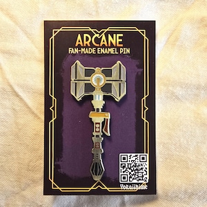 May include: A fan-made enamel pin with a hammer design. The pin is gold, grey, and black, with the word "ARCANE" and "FAN-MADE ENAMEL PIN" printed on the card. A QR code and the name "Yokaiihime" are also visible on the card.