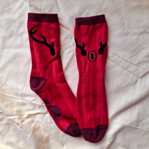 May include: A pair of red socks with black reindeer antlers and the word "Joy" printed on them.