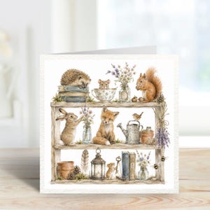 Peut inclure: Une carte de vœux carrée présentant une illustration à l'aquarelle d'une étagère en bois à trois niveaux. L'étagère présente des animaux des bois, dont un hérisson, une souris, un lapin, un renard et un écureuil, avec des fleurs, des livres.