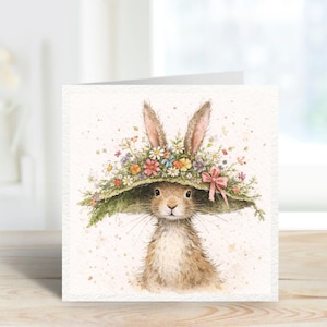 May include: A watercolour illustration of a rabbit wearing a large green hat decorated with colourful flowers and a pink bow. The rabbit has long ears and soft, brown fur. The image is on a white card, suitable for Easter or spring.