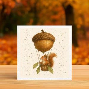 May include: A whimsical square card featuring a watercolor illustration of a red squirrel in a basket, suspended beneath a brown acorn-shaped hot air balloon. The background is a soft beige with subtle speckles, evoking a sense of autumn.
