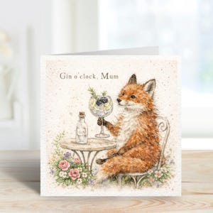 May include: Greeting card featuring a watercolor illustration of a fox enjoying a gin cocktail. The fox is seated at a small table with a bottle of gin and a glass of the cocktail. The card is decorated with flowers and the text "Gin o'clock, Mum".