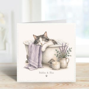 May include: A square greeting card featuring a watercolor illustration of a grey and white cat sleeping in a white clawfoot bathtub. A lavender towel hangs over the side, next to a small candle and a pitcher of lavender sprigs. Text reads Bubbles & Bliss.