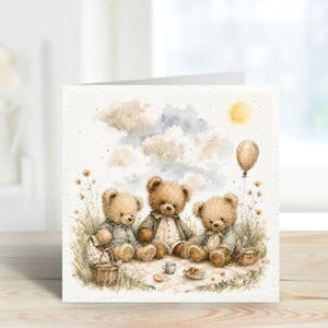 May include: Watercolor greeting card featuring three teddy bears having a picnic. The bears are sitting on a blanket with a basket, tea set, and food. The background includes a yellow sun, a balloon, and a cloudy sky.