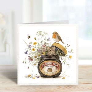 Peut inclure: Carte de vœux carrée avec une illustration. Un pot de "The Pantry Paste" est rempli de fleurs, d'une souris et d'un oiseau. Une abeille vole à proximité. Le texte "Love it or hate it" est sur le pot.