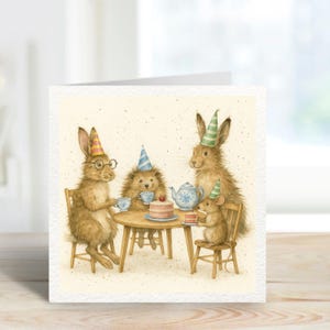 May include: A square greeting card featuring an illustration of a tea party with four woodland creatures. A rabbit wearing glasses and a party hat sits at a small round table with a hedgehog, a rabbit, and a mouse. A cake and tea set are on the table.