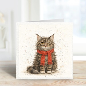 May include: A watercolour illustration of a fluffy tabby cat wearing a bright red scarf. The cat has yellow eyes and is sitting upright. The background is white with subtle speckled accents. The image is on a greeting card.
