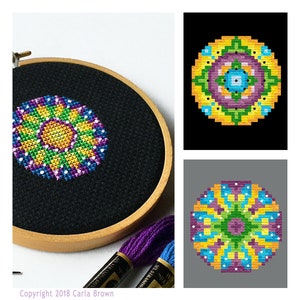 May include: A colorful cross-stitch mandala design with yellow, green, purple, and blue colors. The design is framed in a wooden hoop and is surrounded by embroidery floss.