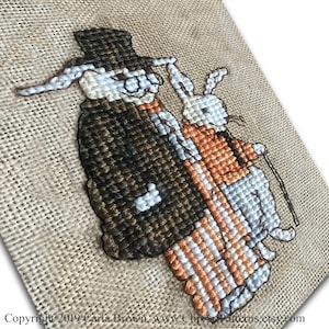 Może przedstawiać: Wzór haftu krzyżykowego przedstawiający dwa króliki ubrane w formalne stroje. Królik po lewej stronie nosi cylinder, brązową kurtkę i spodnie w paski. Królik po prawej stronie nosi pomarańczową kamizelkę i szare spodnie. Oba króliki trzymają laski.