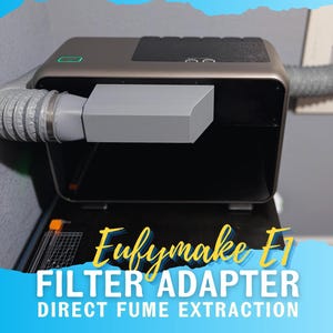 May include: A silver and black Eufymake F1 filter adapter for direct fume extraction. The device has a rectangular shape with a gray rectangular attachment and a flexible gray hose. The text "Eufymake F1 FILTER ADAPTER DIRECT FUME EXTRACTION" is displayed.