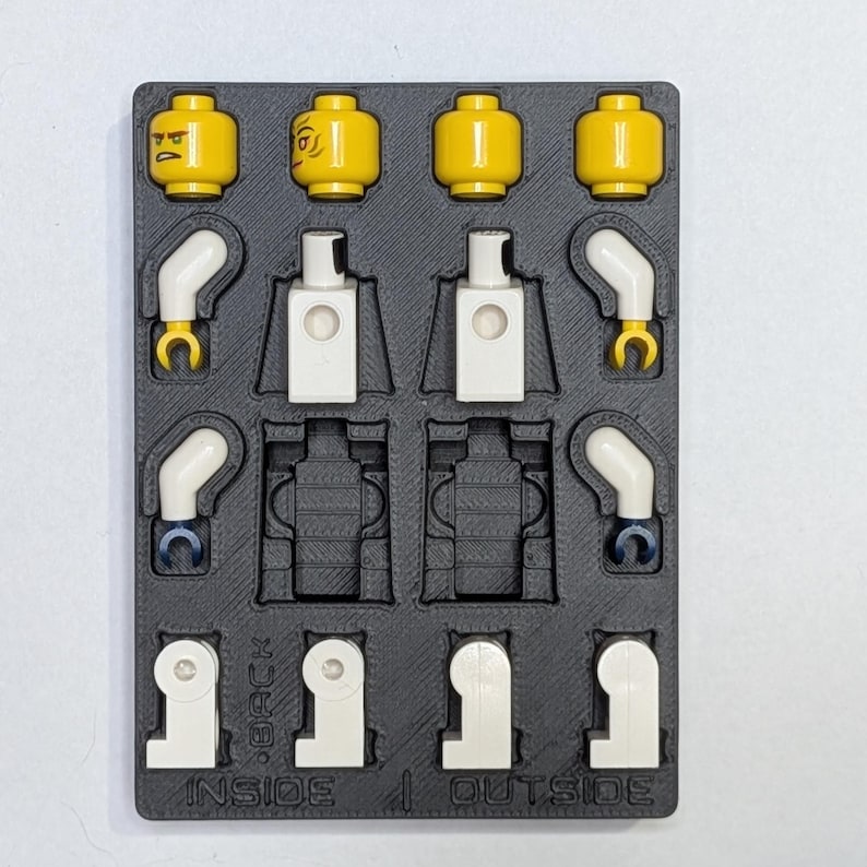 May include: A black plastic organizer tray holding disassembled yellow Lego minifigure heads, white torsos, and arms. The tray is labeled with "INSIDE" and "OUTSIDE" text.