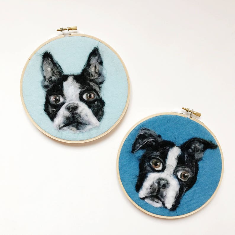 May include: Two needle felted portraits of Boston Terrier dogs in wooden embroidery hoops. The dog on the left is on a light blue background and the dog on the right is on a blue background.