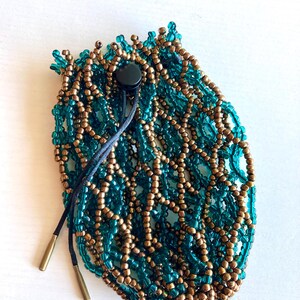 May include: A beaded pouch in teal and bronze colors. The pouch is made of small beads woven together in a net-like pattern. It has a drawstring closure with a black toggle and two gold-colored metal tips.