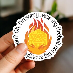May include: White sticker featuring a yellow D20 die surrounded by orange and yellow flames. The text on the sticker reads "Oh, I'm sorry... was my fireball not big enough?" in a black, circular font.