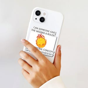 May include: White phone case with a sticker featuring a yellow 20-sided die engulfed in flames. The sticker has the text "CAN SOMEONE GIVE THE WIZARD A RULER..." and "GENERAL CONCEPT COURTESY?"