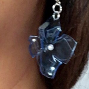 May include: A pair of blue flower-shaped earrings with a silver hook and a small pearl accent.