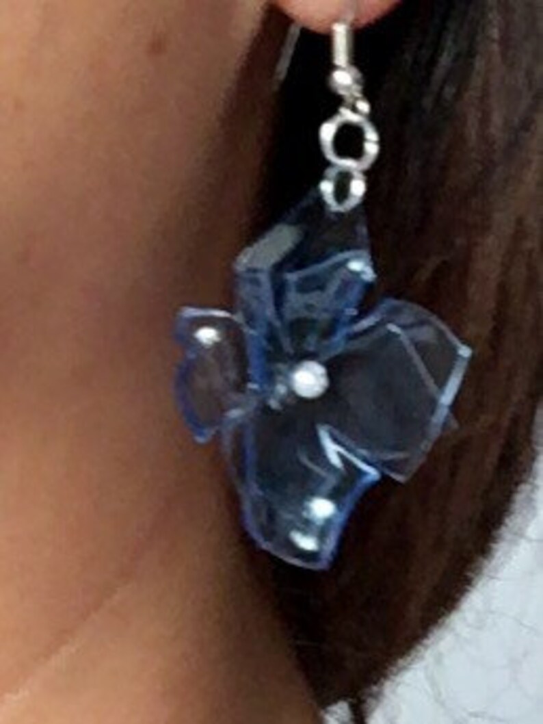 May include: A pair of blue flower-shaped earrings with a silver hook and a small pearl accent.