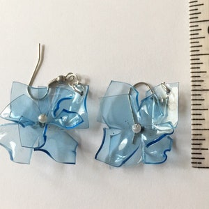 May include: A pair of blue plastic flower earrings with silver hooks. The earrings are approximately 2.5 cm in diameter.