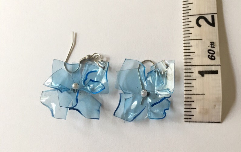 May include: A pair of blue plastic flower earrings with silver hooks. The earrings are approximately 2.5 cm in diameter.