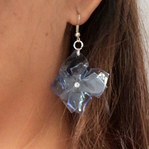 May include: A pair of blue flower-shaped earrings with a silver hook and a clear rhinestone in the centre.