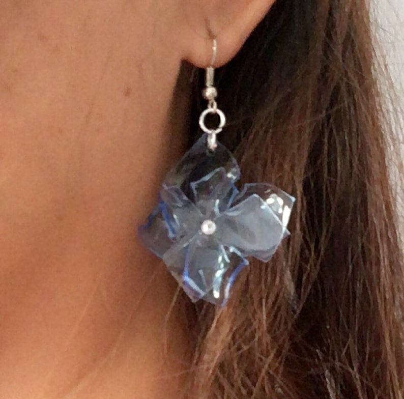 May include: A pair of blue flower-shaped earrings with a silver hook and a clear rhinestone in the centre.