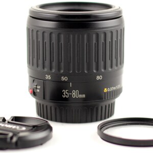 May include: A black Canon EF 35-80mm f/4-5.6 lens with a black lens cap and a black filter ring. The lens has a zoom ring and a focus ring. The lens is designed for Canon EOS cameras.