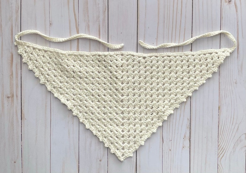 May include: A white crocheted triangular scarf with a scalloped edge.