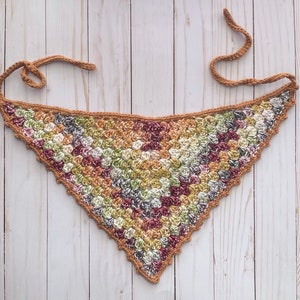 May include: A crocheted triangular scarf in a brown, green and pink colour scheme. The scarf is made with a textured stitch and has a fringed edge.