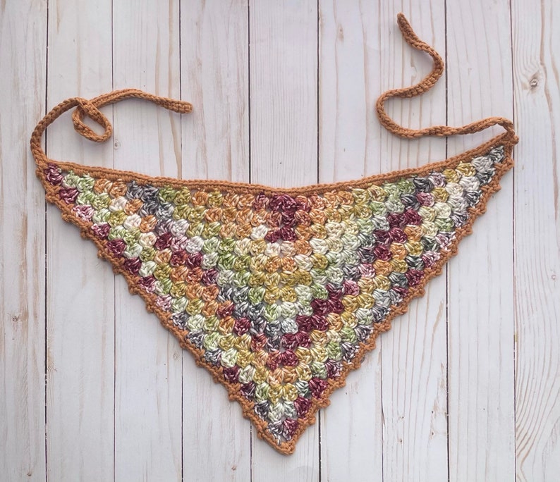 May include: A crocheted triangular scarf in a brown, green and pink colour scheme. The scarf is made with a textured stitch and has a fringed edge.