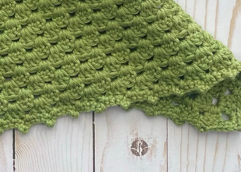 May include: A close-up of a green crocheted fabric with a scalloped edge.