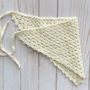 May include: A white crocheted triangular scarf with a long tie. The scarf is made with a delicate stitch pattern and has a scalloped edge.