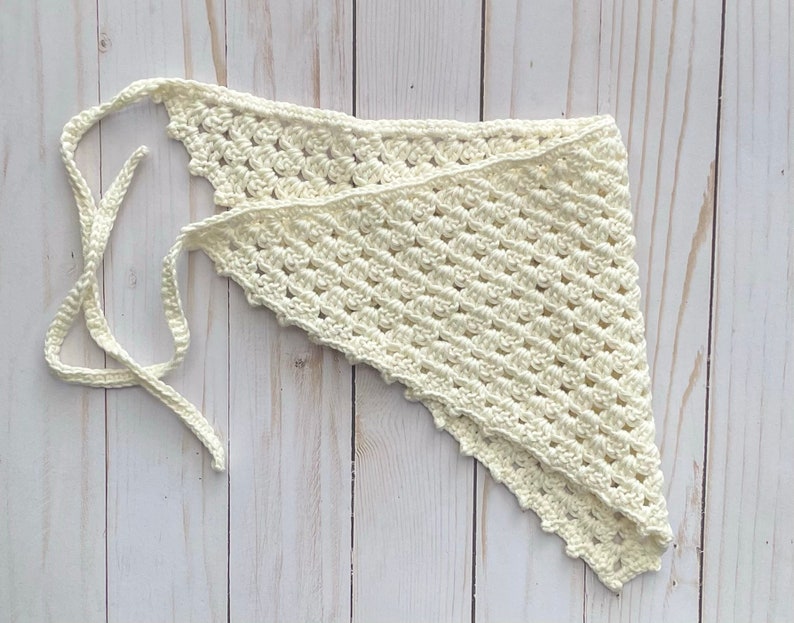 May include: A white crocheted triangular scarf with a long tie. The scarf is made with a delicate stitch pattern and has a scalloped edge.