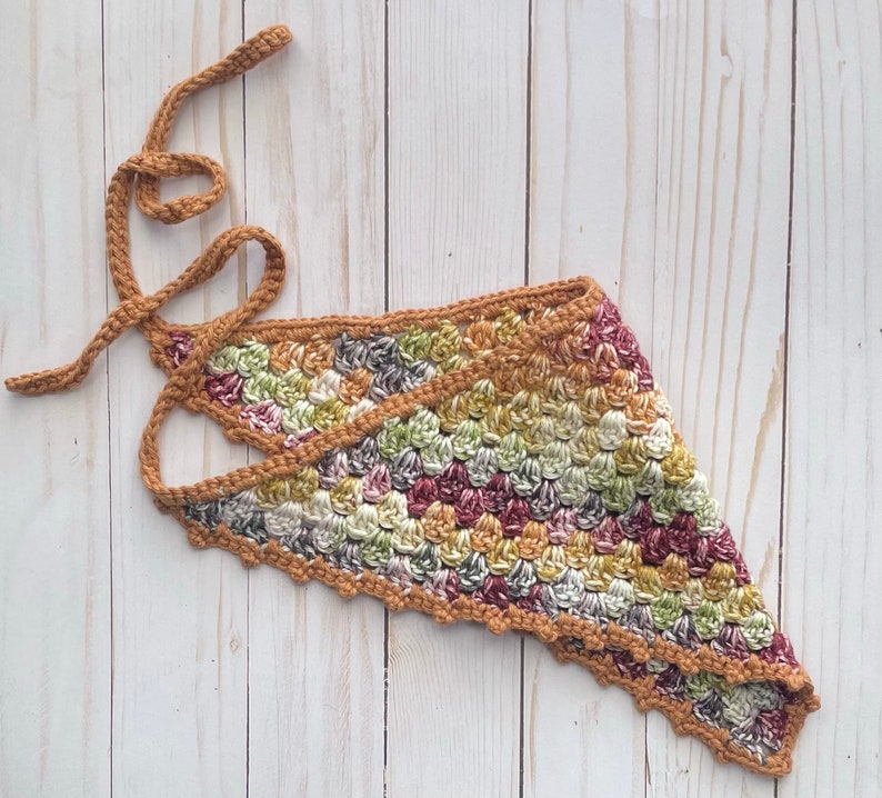 May include: A crocheted triangular scarf with a scalloped edge in shades of brown, green, and pink. The scarf has a long brown cord attached to it.
