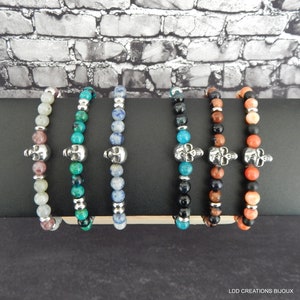 Peut inclure: Six bracelets en perles avec des breloques en forme de crâne argenté. Les bracelets sont faits de pierres de différentes couleurs, notamment le vert, le bleu, le noir, le marron et l'orange.