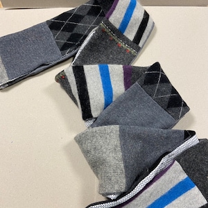 May include: A gray, black, and white striped scarf with a blue stripe. The scarf is made of a soft, knitted fabric and has a patchwork design.