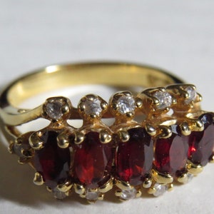 May include: A gold ring with a row of five red gemstones surrounded by smaller clear gemstones.