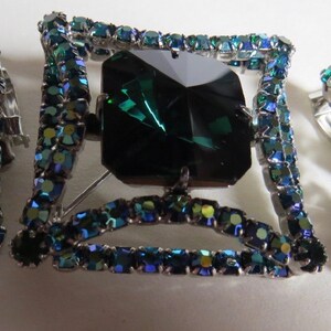 Puede incluir: Un conjunto de joyas de pedrer&iacute;a verde esmeralda y azul con un broche cuadrado con una gran piedra verde esmeralda y pendientes de clip a juego.