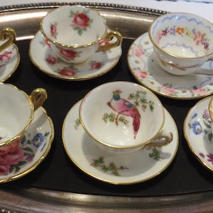 May include: Set of six miniature teacups and saucers with floral and bird designs. The cups and saucers are white with gold trim and feature colorful floral and bird motifs.